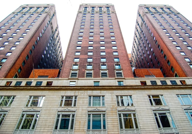 Exterior shot looking up at a building covered in windows with white walls on the first few stories and then red brick going up from there. 