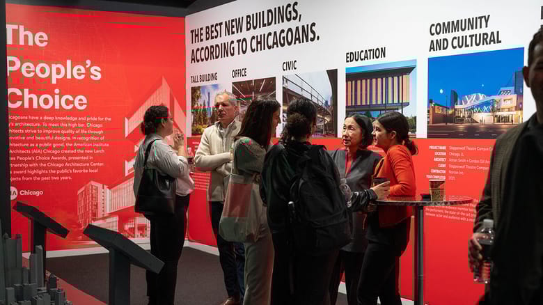 A group of people standing around in an exhibit space and chatting.