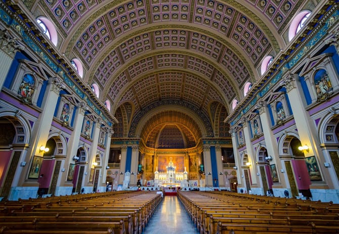 Inside of a dimly lit church with symmetrical pews and lit altar in focus