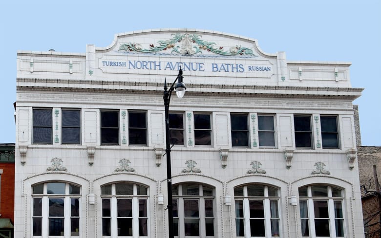 White window lined building with green embellishmnets and a sign with blue text on top that reads "North Avenue Baths"