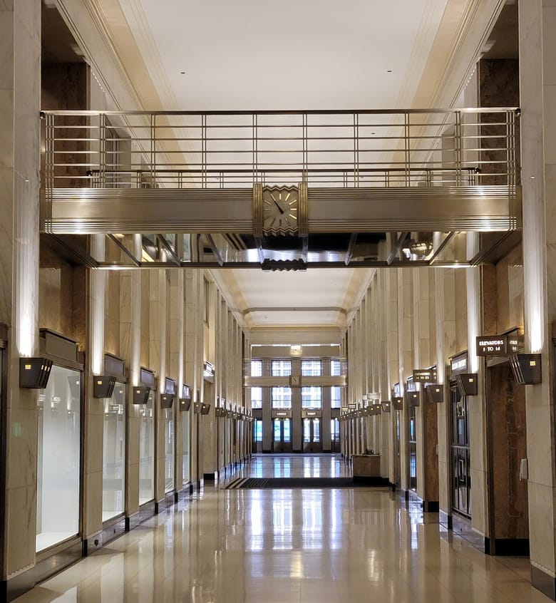 Long hallway with light reflecting off the marble walls and floors and sconces lighting the space. 