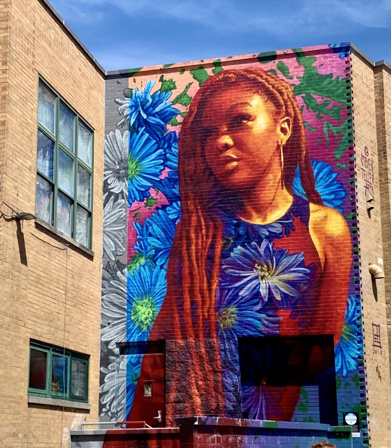 Mural of a young black woman with flowers everywhere on the side of a building