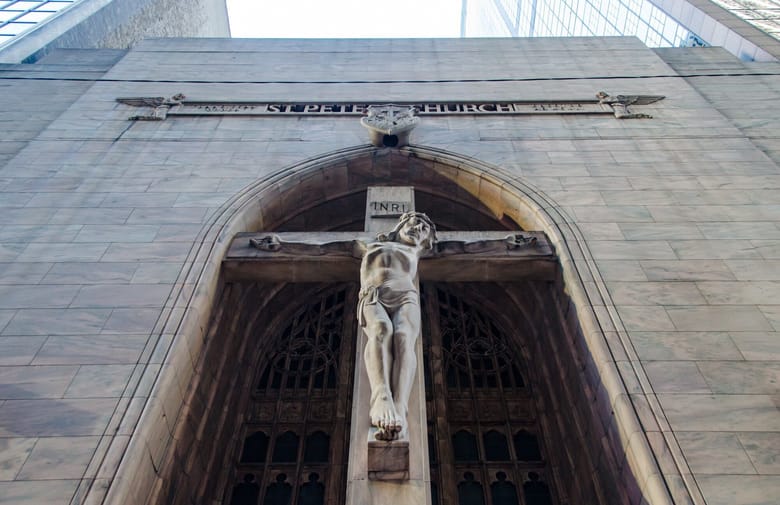 Image looking up at a sculpture carved in stone of Jesus with his arms spread across a cross