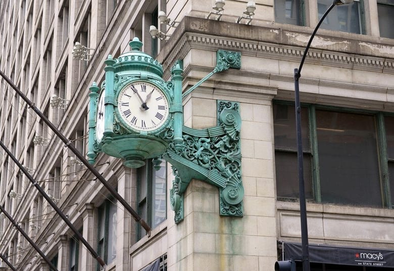 Exterior of an old building focused on a green clock hanging from the corner.