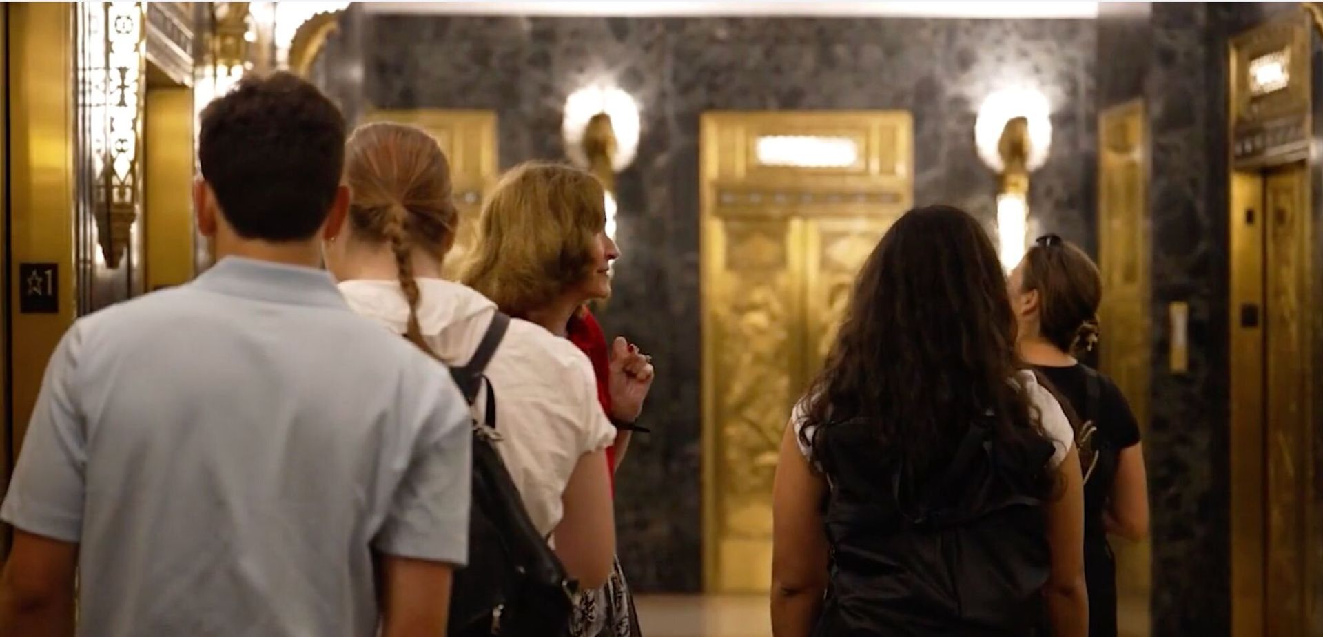 Tour group in an art deco building interior with gold elevator doors