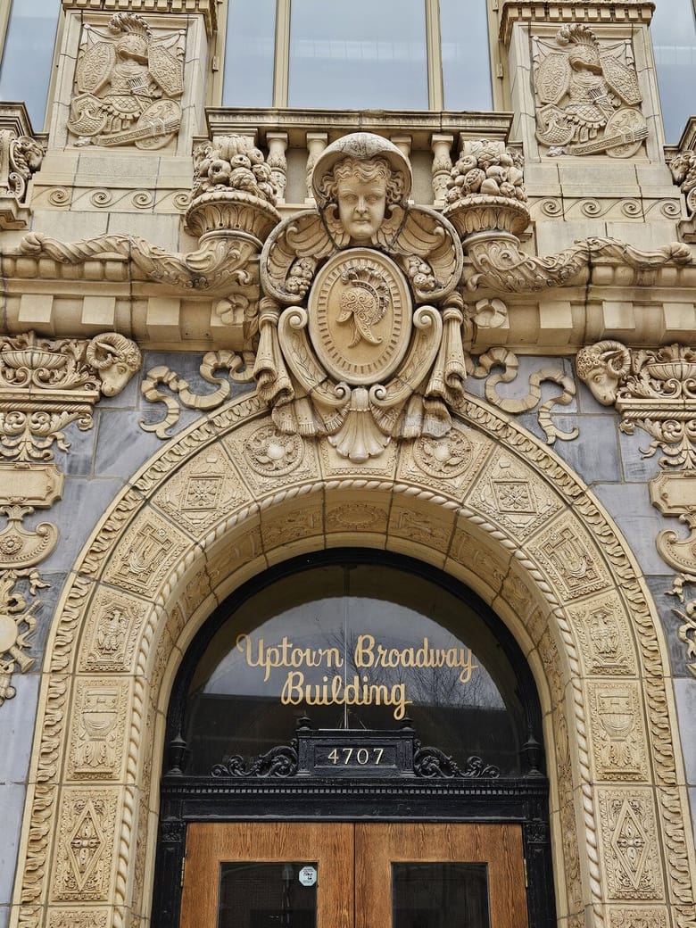 Exterior view of a brick building with ornate scultures with the words Uptown Broadway Building etched on glass