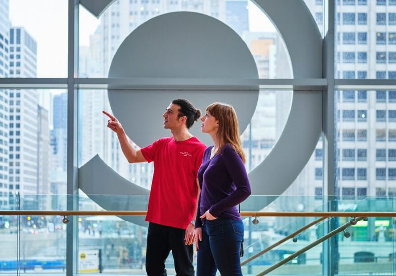 Two people with the CAC logo in behind them in a window. They are looking left and one is pointing.